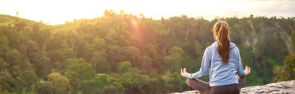 Image of young woman sitting cross-legged on rock overlooking a forest